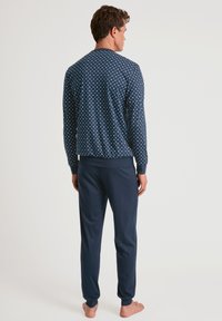 Marineblauwe pyjama-set met een gestippelde lange mouw top met ribgebreide boorden en bijpassende broeken met elastische tailleband en taps toelopende pijpen.