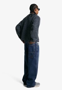 Sivi, fluffy pulover u kombinaciji sa širokim tamnim trapericama. Outfit se odlikuje opuštenim krojem i suptilnim detaljima šivanja.