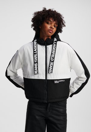 Zwart-witte puffjas met een capuchon, voorzien van opvallende logostrepen en een ritsluiting. Inclusief contrasterende panelen en elastische manchetten.