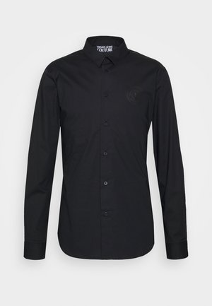 Zwarte blouse met lange mouwen, knoopsluiting en puntige kraag, met subtiel reliëflogo op de linkerborst van Versace Jeans Couture.