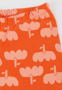 Orange fabric featuring a repeating pattern of light pink flowers with stems and leaves. Soft, stretchy material with an elastic waistband.