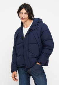 Chaqueta de plumas navy con capucha, que cuenta con un cierre frontal con cremallera, botones a presión, grandes bolsillos y acentos de panel texturizado.