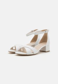White high-heel sandals with an ankle strap, featuring crossed front bands, smooth leather material, and a chunky block heel.