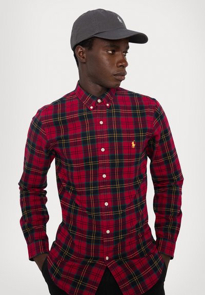 Κόκκινο και ναυτικό καρό πουκάμισο με κουμπιά, μακριά μανίκια και λευκά κουμπιά, με μικρό κεντημένο λογότυπο στο στήθος. Γκρίζο καπέλο.