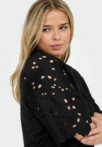 Black blouse featuring intricate lace sleeves with floral cut-out patterns, soft texture, and a relaxed fit.