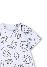 Cămașă albă cu mâneci scurte, având un desen în linii negre cu figuri cu căști, cu închidere cu capse la umăr. Textul spune „KARL LAGERFELD.”