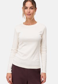 Camicia di cotone color crema a maniche lunghe con scollatura ondulata, design aderente e texture liscia. Abbinata a pantaloni scuri.