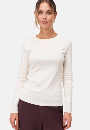 Chemise en coton crème à manches longues avec un décolleté festonné, un design près du corps et une texture lisse. Associée à un pantalon sombre.