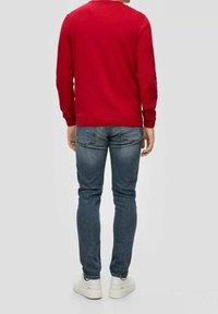 Rode trui met lange mouwen, ronde hals en geribbelde manchetten, gecombineerd met slim-fit blauwe jeans en witte sneakers. Achteraanzicht weergegeven.