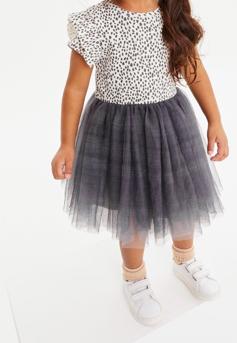 Robe à manches courtes avec un haut blanc orné d'un motif à pois noirs et une jupe en tulle grise. Des baskets blanches et des chaussettes en tricot pêche complètent la tenue.