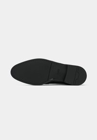 Semelle de chaussure de ville noire avec marquage "Boss", coutures visibles et forme lisse et pointue sur un fond clair uni.