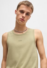 Débardeur côtelé kaki avec encolure ras du cou et logo HUGO sur la poitrine, superposé avec un collier en perles à plusieurs brins.