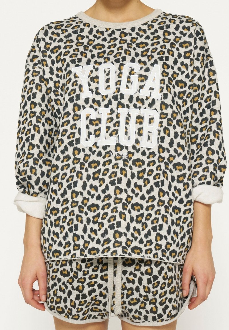 Sudadera con estampado de leopardo y texto blanco "YOGA CLUB". Presenta mangas largas y un corte relajado, hecha de una tela suave con puños enrollados.