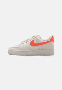 Zapatillas Nike Air Force 1 en cuero beige claro con un acabado texturizado y detalles en naranja brillante. Punta redondeada, cordones planos, suela de goma.