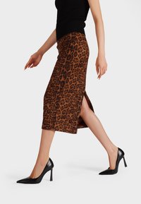 Gonna midi con stampa leopardata in marrone e nero, con uno spacco laterale, abbinata a tacchi a punta neri. Texture liscia, silhouette aderente.
