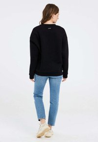 Felpa nera con una vestibilità rilassata, scollo rotondo e maniche lunghe, abbinata a jeans azzurri e sneakers crema.
