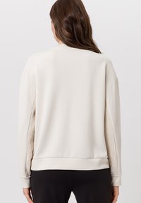 Lichtbeige sweatshirt met geribbelde accenten langs de mouwen, een losse pasvorm, ronde halslijn en een zachte textuur, ontworpen voor comfort en draaggemak.