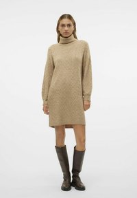 Abito maglione in beige chiaro, con colletto alto, maniche lunghe e motivo a rombi. Abbinato a stivali marroni alti fino al ginocchio.