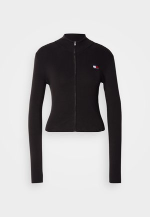 Svart zip-up genser med høy hals, lange ermer, tettsittende design, ribbet tekstur, og et lite logo-patch på venstre bryst.