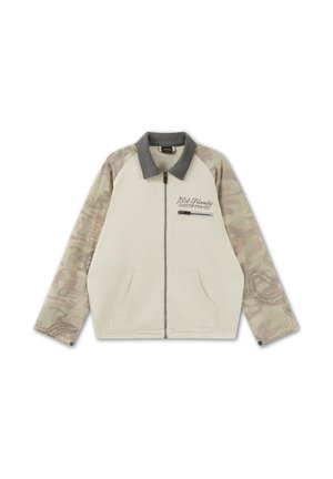 Beige jas met rits en grijze kraag, mouwen met camouflagepatroon, zakken aan de voorkant en "Ed Hardy 1974" geborduurd nabij het borstzakje met rits.