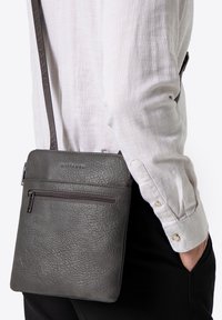 Graue Leder-Umhängetasche mit strukturierter Oberfläche, ausgestattet mit einer vorderen Reißverschlusstasche und einem verstellbaren Riemen für mehr Komfort.