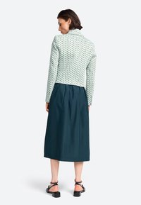 Jachetă cu un model verde și alb, cu un design ajustat, purtată cu o fustă bleumarin, lungime la genunchi și sandale negre cu bretele.