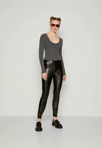 Gray long-sleeve bodysuit, black leather pants, and black platform shoes. Model wears rectangular sunglasses and has styled hair in two buns.