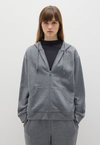 Grijze hoodie met rits, gemaakt van zachte stof, met een rits aan de voorkant, twee zakken en een capuchon met koordjes; gecombineerd met bijpassende joggingbroek.