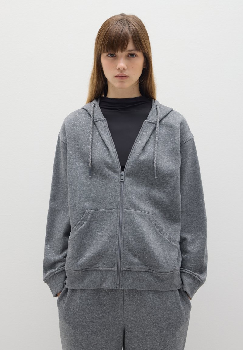 Grijze hoodie met rits, gemaakt van zachte stof, met een rits aan de voorkant, twee zakken en een capuchon met koordjes; gecombineerd met bijpassende joggingbroek.