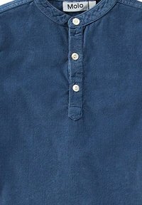 Blå kord skjorta med rund halsringning, som har en knappslå med tre vita knappar och en mjuk, texturerad yta.
