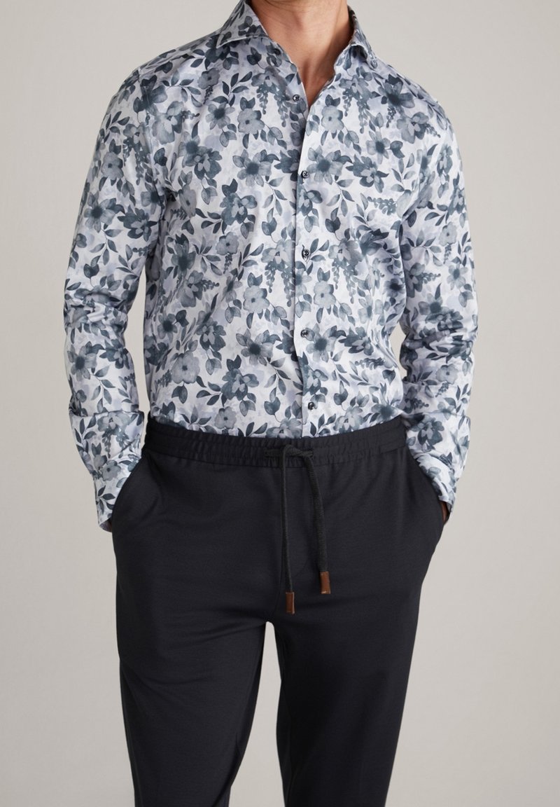 Koszula w kwiaty z długim rękawem w niebiesko-białe wzory, z kołnierzykiem zapinanym na guziki oraz misternymi wzorami liści i kwiatów; zestawiona z czarnymi spodniami na sznurki.