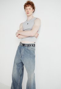 Hallitatud hall sleeveless top, kõrge vöökoht kerge sinise laia jalgadega teksad, must vöö hõbedaste ümmarguste detailidega, mudel seisab valge tausta ees.