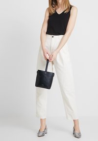 Black sleeveless top, white high-waisted trousers, black mini handbag, reptile-patterned heels. Focus on materials and clean lines.