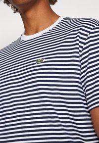 T-shirt en coton à rayures bleu marine et blanches avec un col rond en ribécourt blanc et un petit logo crocodile brodé en vert sur la poitrine.