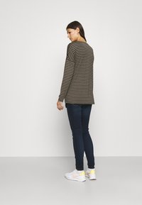 Camisola de mangas longas, verde-oliva com riscas, de corte descontraído. Combinada com jeans skinny azul-escuro e ténis brancos com detalhes amarelos.