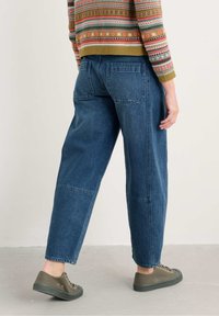 Donkerblauwe denim straight-leg jeans met zijzakken, zichtbare stiksels, gedragen met groene canvas sneakers. Gestructureerde stof.