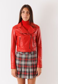 Giubbotto da biker in pelle rossa, corto, con cerniere e colletto a punte, abbinato a una gonna a pieghe grigia a scacchi con accenti rossi.