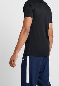 Svart kortärmad träningsskjorta med en åtsittande design och andningsbart material, tillsammans med marinblå byxor med vita sidestreck.