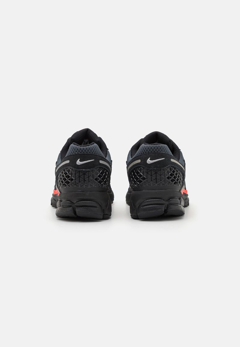 Chaussures de sport noires avec une tige en maille, présentant des accents gris et rouge, des panneaux texturés et une semelle en caoutchouc durable avec un talon rembourré.