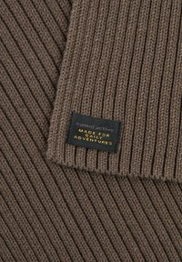 Bruine geribbelde sjaal gemaakt van gebreide stof met een gestructureerde uitstraling. Bevat een zwart etiket met de tekst "cameractive MADE FOR DAILY ADVENTURES."