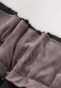 Gros plan d’un tissu avec des coutures texturées marron sur un matériau élastique noir montrant des coutures et des plis détaillés.