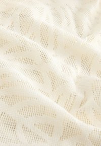 Tissu en dentelle ivoire avec des motifs floraux et une texture en maille à grille, présenté en plis doux et en gros plan.