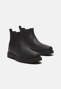 Botas Chelsea de cuero negro con paneles laterales elásticos, lengüetas de tiro y suelas de goma resistentes. Textura suave y diseño de punta redondeada.