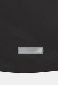 Černá textilní taška s obdélníkovou šedou štítkou s reliéfním textem. Hladká textura s jednoduchým designem.