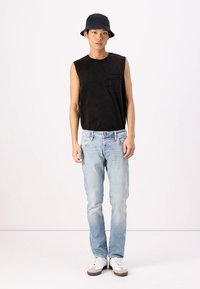 Top sin mangas negro, jeans de color azul claro, zapatillas blancas con detalles marrones y un sombrero tipo bucket negro. Un atuendo sencillo y casual con un corte relajado.