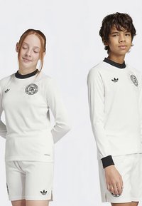 White long-sleeve athletic tops with black accents and logos paired with matching white shorts. Ribbed texture throughout the fabric.