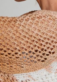 Haut en crochet présentant un motif à maille ouverte dans des nuances de pêche et de crème, avec un fil texturé et un design superposé à l'ourlet.