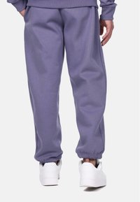Purple sweatpants with elastic cuffs, made of soft fabric. Worn with white sneakers, featuring a relaxed fit and side pockets.