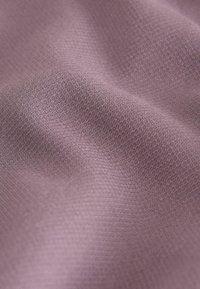 Zbliżenie na teksturowaną fioletową tkaninę ukazującą wzór tkany oraz miękkie fałdy tworzące subtelne cienie i refleksy światła.