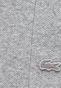 Gros plan sur un tissu gris tricoté avec une couture visible et un petit logo alligator brodé dans des tons gris assortis.